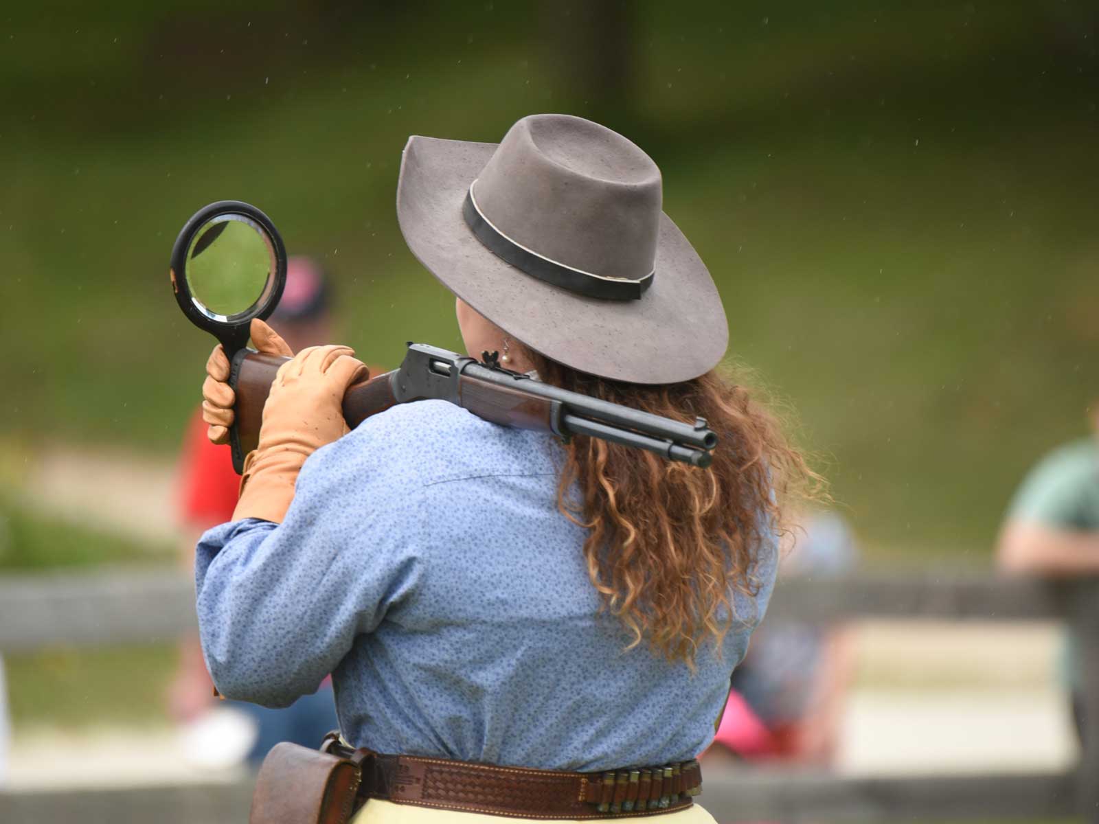 woman holding a mirror and gun for a behind-the-back trick shot at the Buffalo Bill Wild West Show